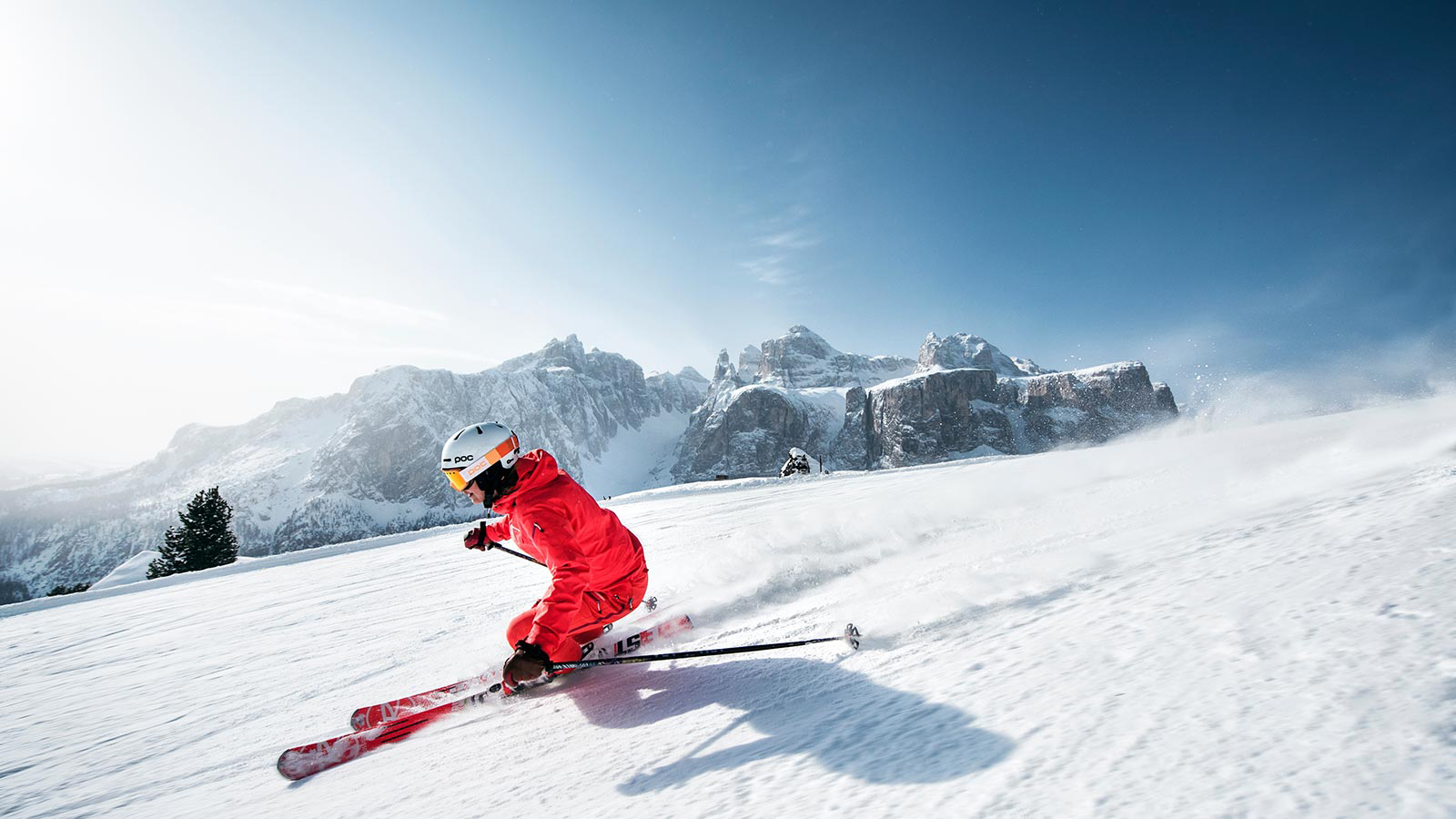 A skier descends fast on the slopes with the Dolomites in the background