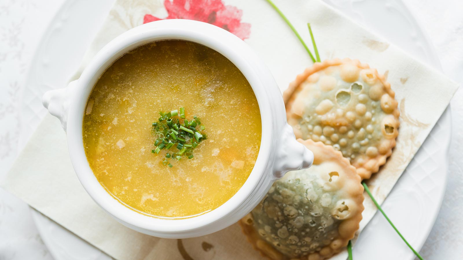A cup of steaming broth with delicacies with spinach on the side